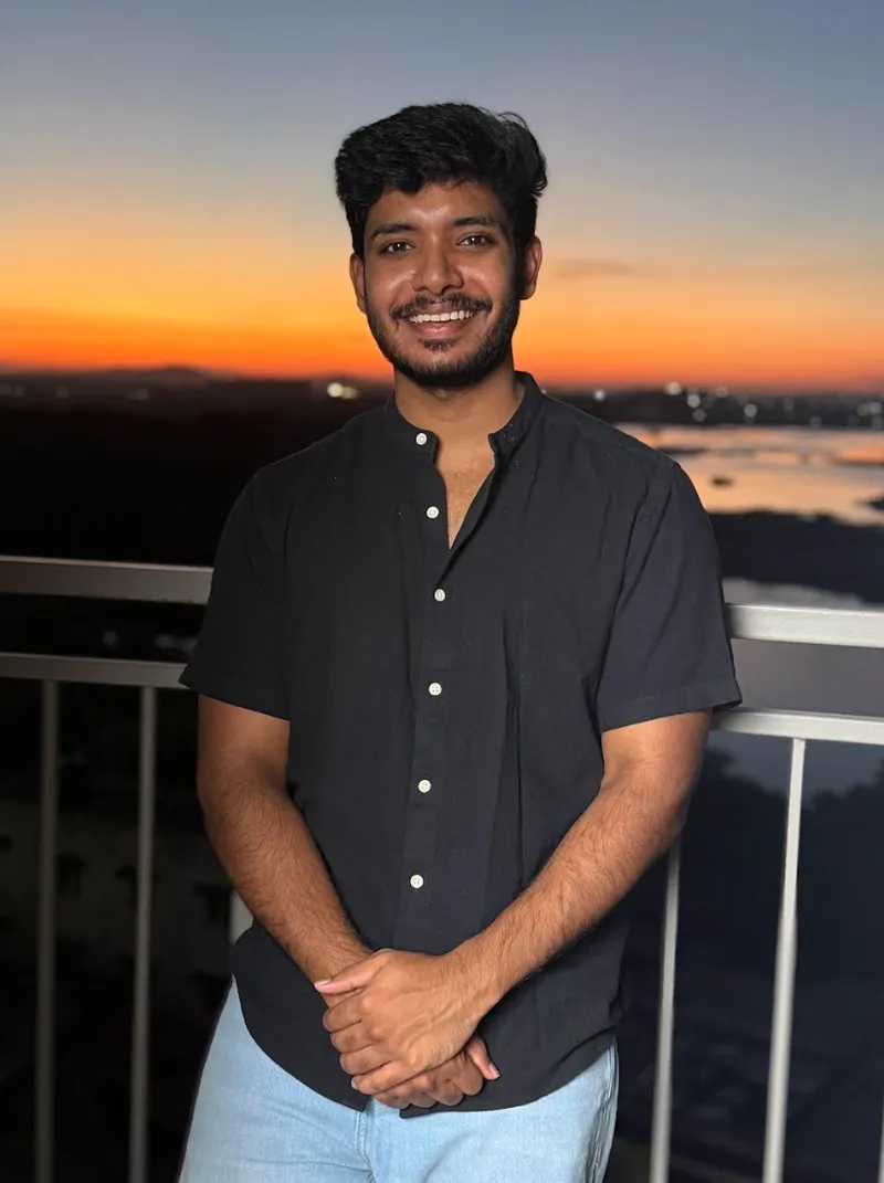 Epaphra standing beside a balcony railing at sunset, wearing a dark shirt.